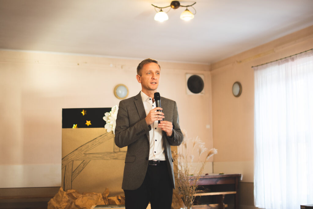 Pan Karol Bruzda stoi na scenie i składa świąteczne życzenie uczestnikom. 