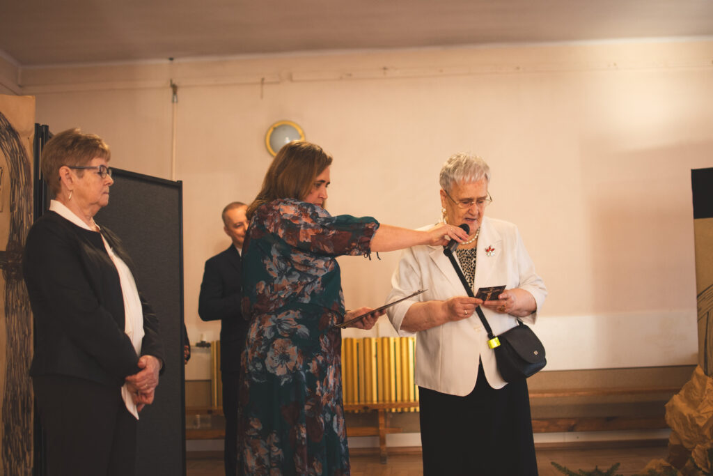 Kobiety stojące na scenie. Jedna z Seniorek odczytuje modlitwę. 